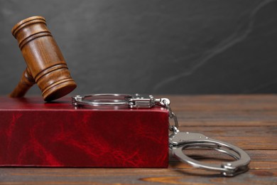 Book, judge's gavel and handcuffs on wooden table against gray background, space for text