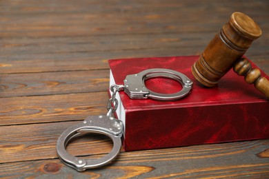 Book, judge's gavel and handcuffs on wooden table, closeup. Space for text