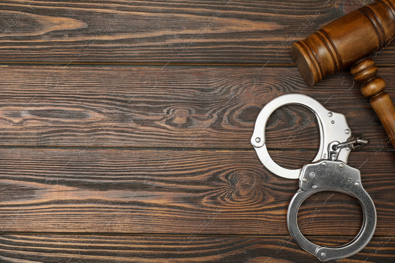 Photo of Judge's gavel and handcuffs on wooden table, flat lay. Space for text