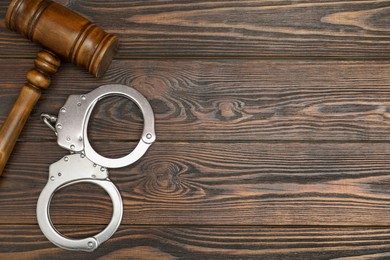 Photo of Judge's gavel and handcuffs on wooden table, flat lay. Space for text