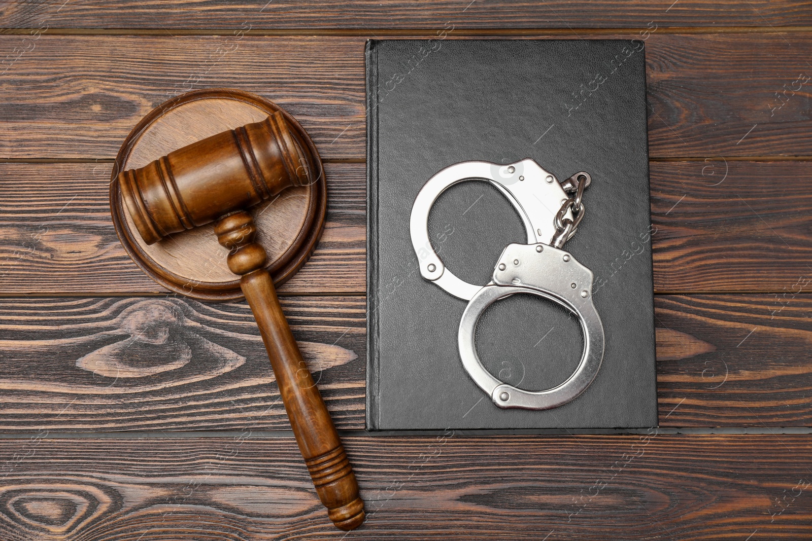 Photo of Book, judge's gavel and handcuffs on wooden table, flat lay