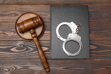 Book, judge's gavel and handcuffs on wooden table, flat lay