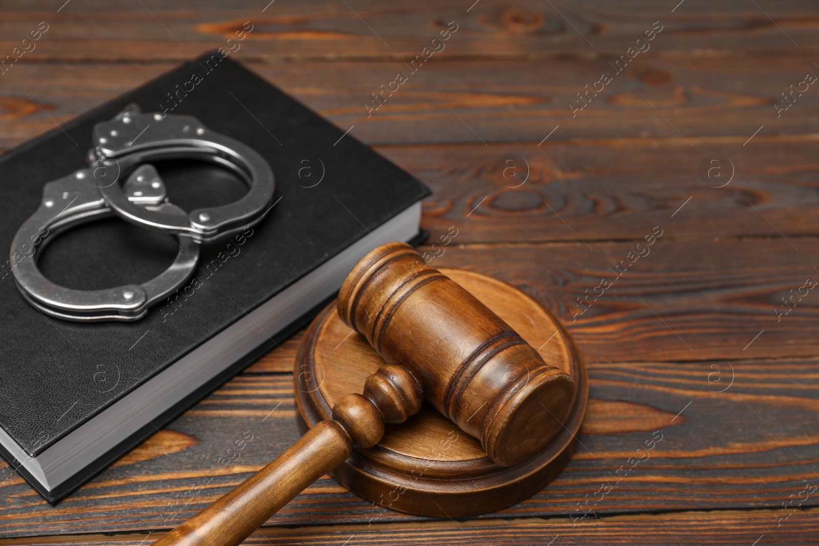 Photo of Book, judge's gavel and handcuffs on wooden table, closeup. Space for text