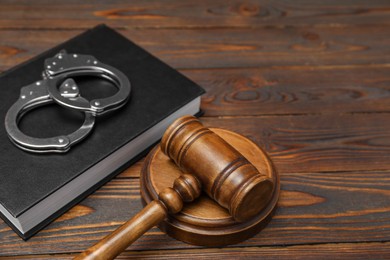 Book, judge's gavel and handcuffs on wooden table, closeup. Space for text