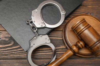 Photo of Book, judge's gavel and handcuffs on wooden table, flat lay