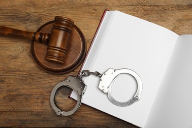 Book, judge's gavel and handcuffs on wooden table, flat lay