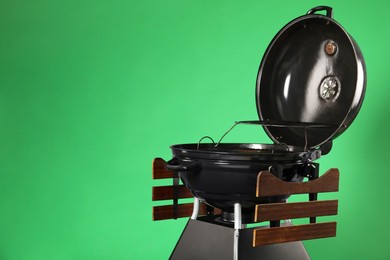 Photo of One black barbeque grill against green background. Space for text