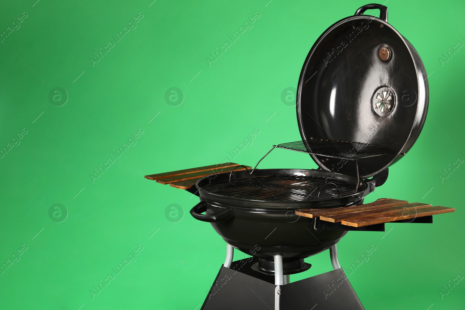 Photo of One black barbeque grill against green background. Space for text