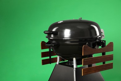 Photo of One black barbeque grill against green background. Space for text