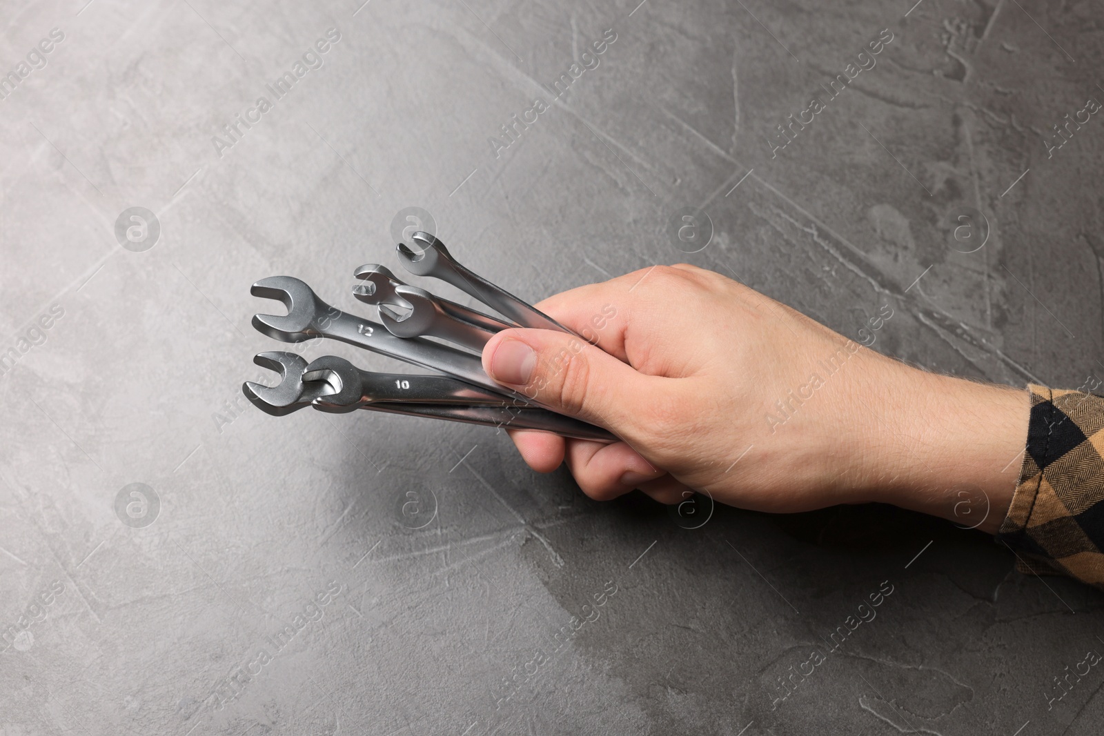 Photo of Auto mechanic with wrenches at grey textured table, closeup