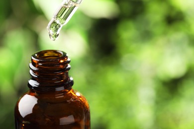 Essential oil dripping from pipette into bottle against blurred green background, closeup. Space for text