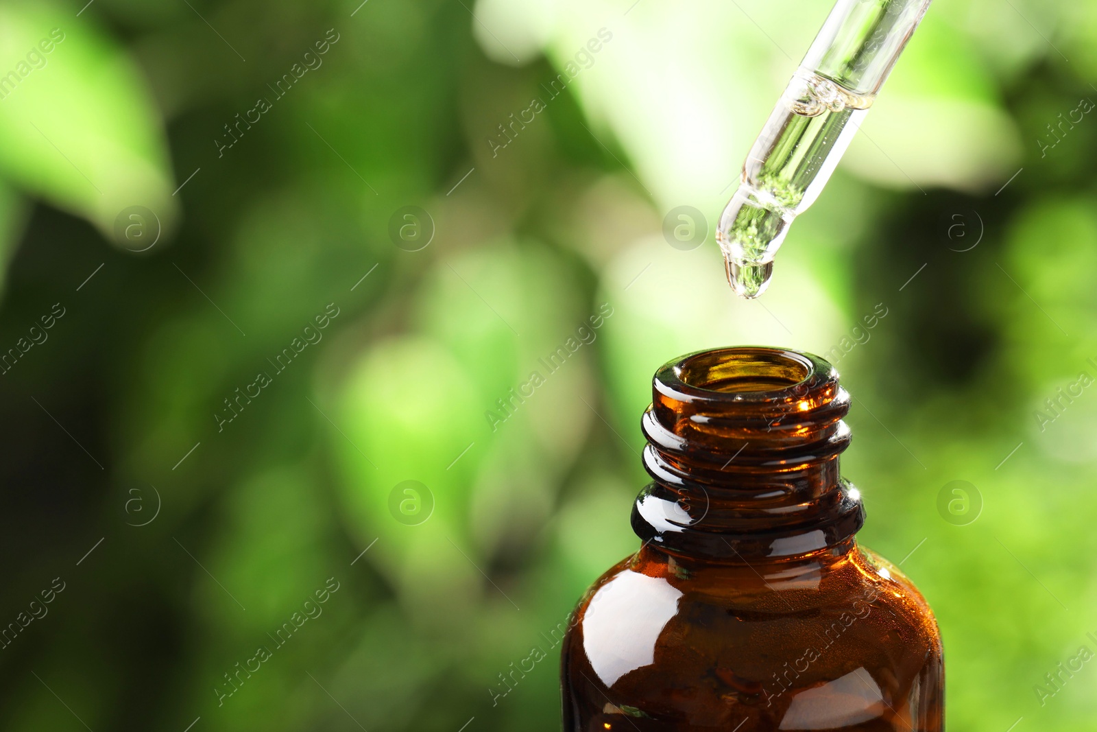 Photo of Essential oil dripping from pipette into bottle against blurred green background, closeup. Space for text