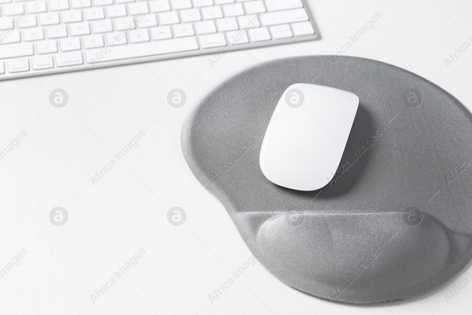 Photo of Keyboard, mouse and mousepad with arm rest on white table, closeup. Space for text