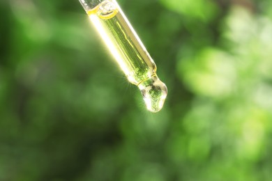 Photo of Essential oil dripping from pipette on blurred background, closeup