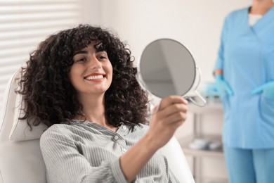 Photo of Patient looking in mirror and doctor in clinic, selective focus. Dental veneers