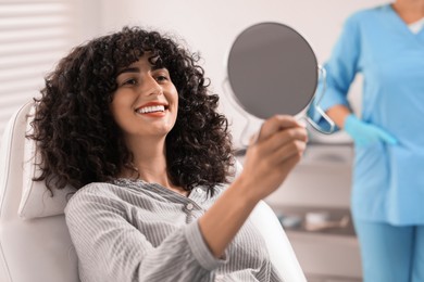 Photo of Patient looking in mirror and doctor in clinic, selective focus. Dental veneers