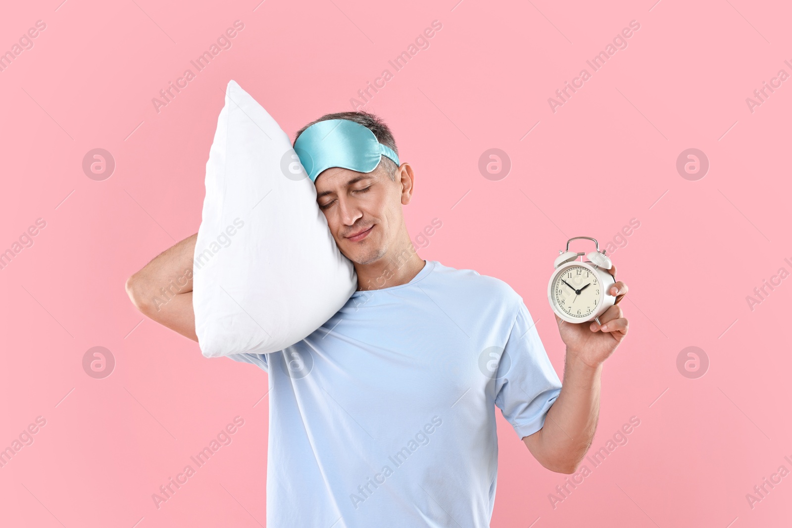 Photo of Overslept man with sleep mask, pillow and alarm clock on pink background