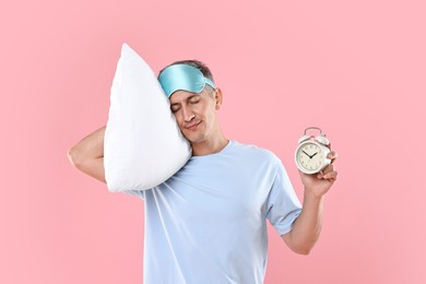 Overslept man with sleep mask, pillow and alarm clock on pink background