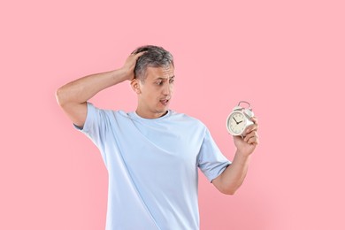 Overslept man with alarm clock on pink background