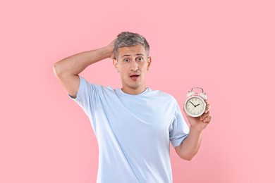 Overslept man with alarm clock on pink background