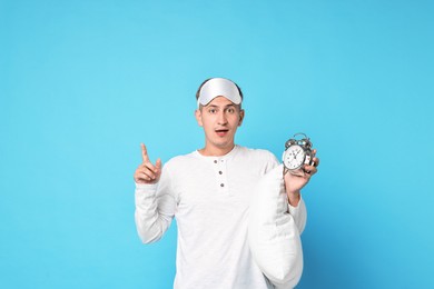 Photo of Overslept man with sleep mask, pillow and alarm clock on light blue background