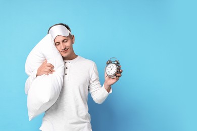 Photo of Overslept man with sleep mask, pillow and alarm clock on light blue background