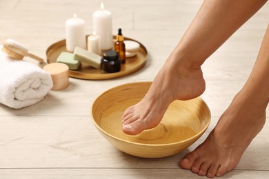 Photo of Woman soaking her feet in bowl with water on floor, closeup. Body care