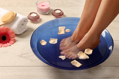 Photo of Woman soaking her feet in bowl with water and petals on floor, closeup. Body care