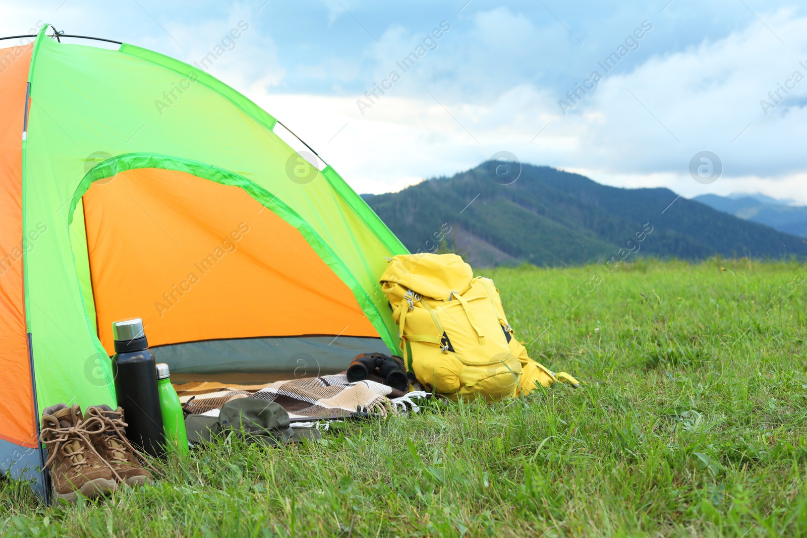 Photo of Tent and backpack on green grass in mountains, space for text