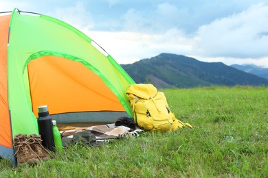 Tent and backpack on green grass in mountains, space for text