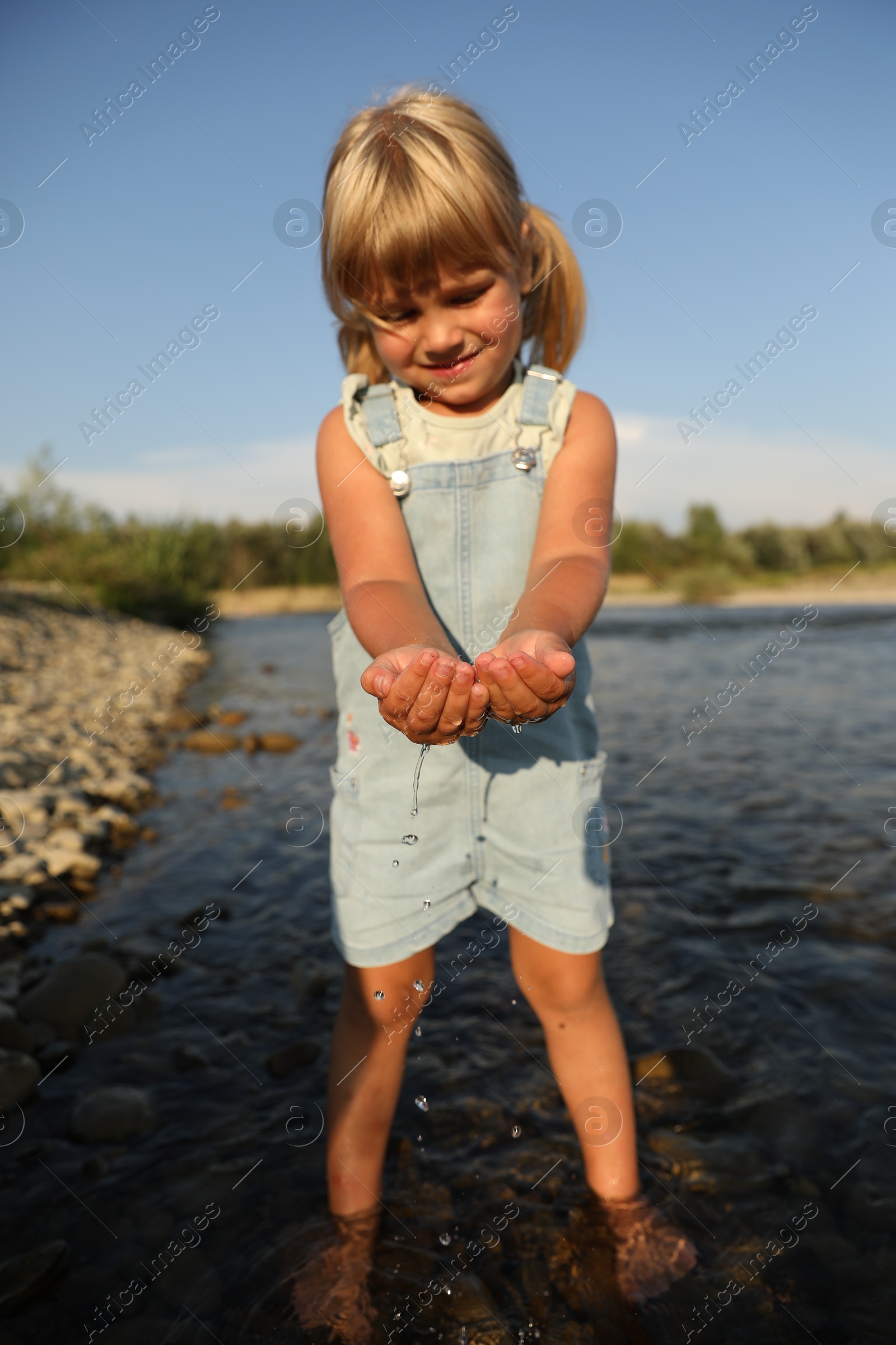 Photo of Cute little girl playing with water near river. Child enjoying beautiful nature