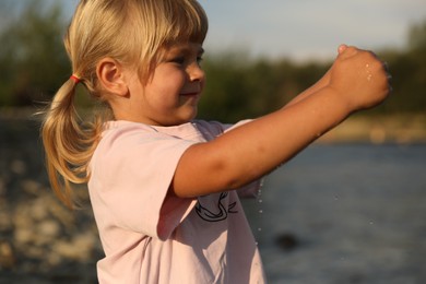 Cute little girl playing with water near river. Child enjoying beautiful nature