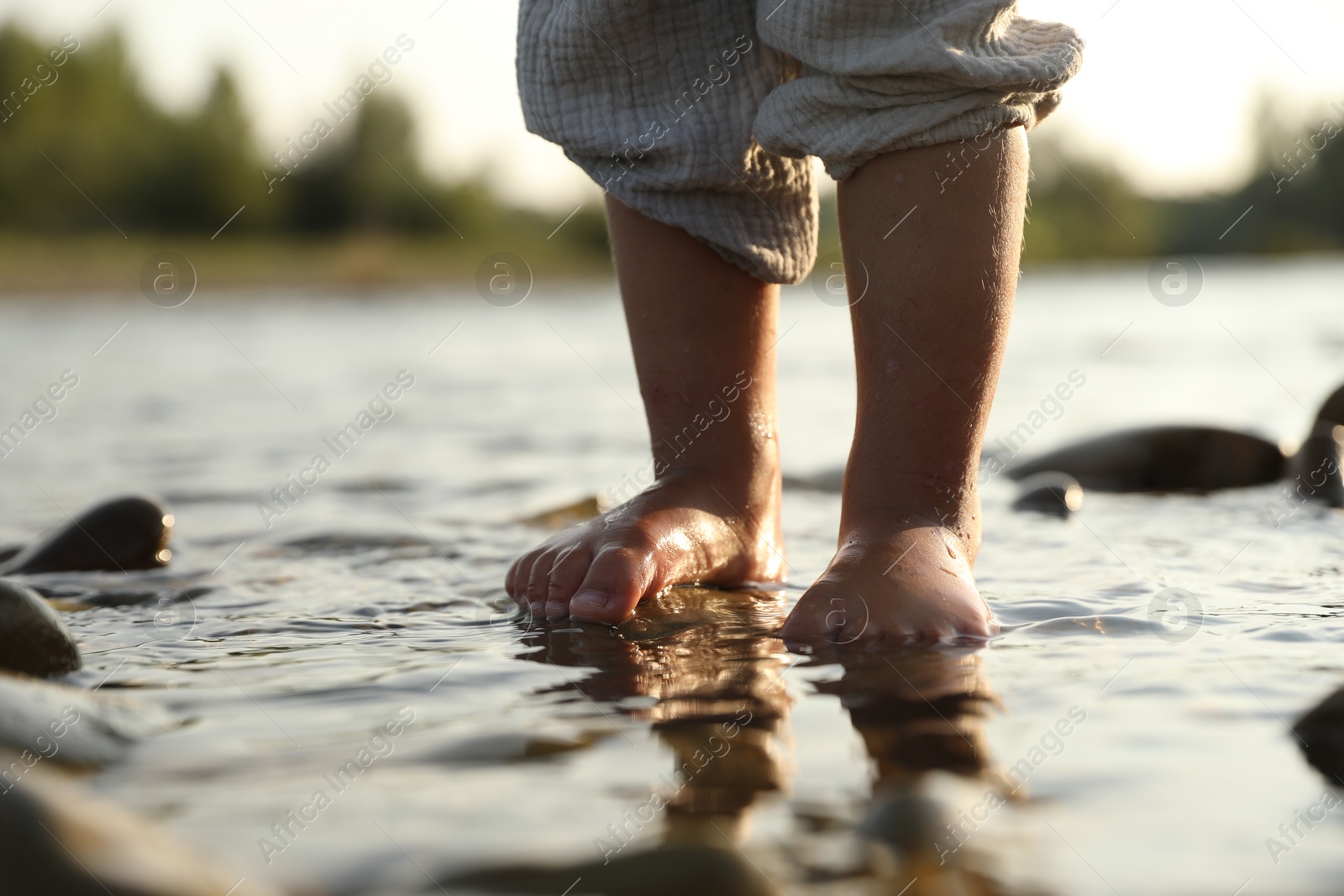 Photo of Cute little girl standing in water outdoors, closeup. Child enjoying beautiful nature