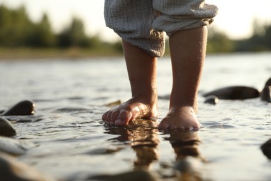 Photo of Cute little girl standing in water outdoors, closeup. Child enjoying beautiful nature