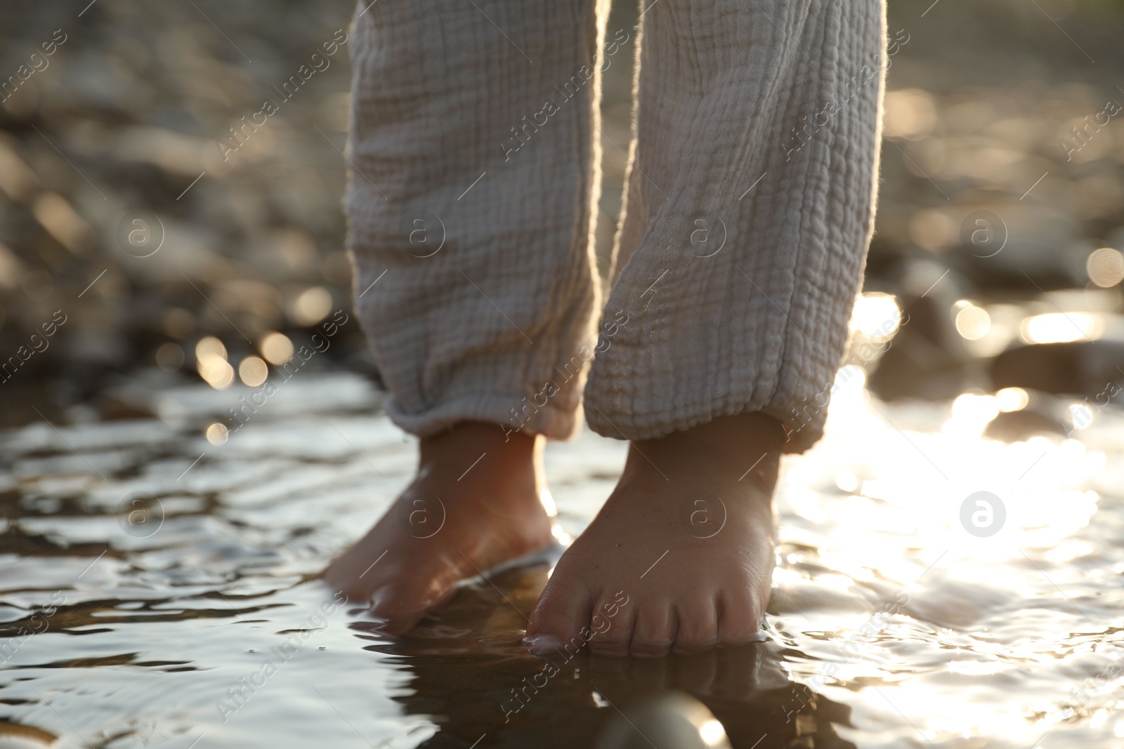 Photo of Cute little girl standing in water outdoors, closeup. Child enjoying beautiful nature