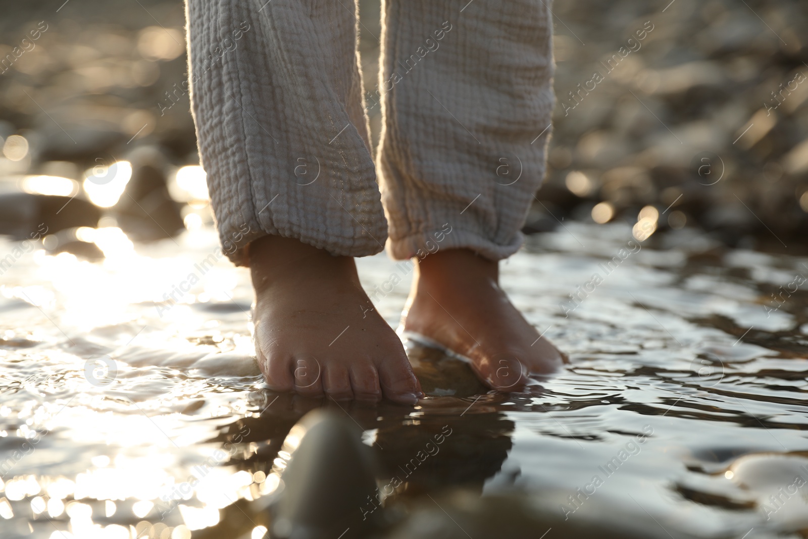 Photo of Cute little girl standing in water outdoors, closeup. Child enjoying beautiful nature