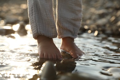 Photo of Cute little girl standing in water outdoors, closeup. Child enjoying beautiful nature