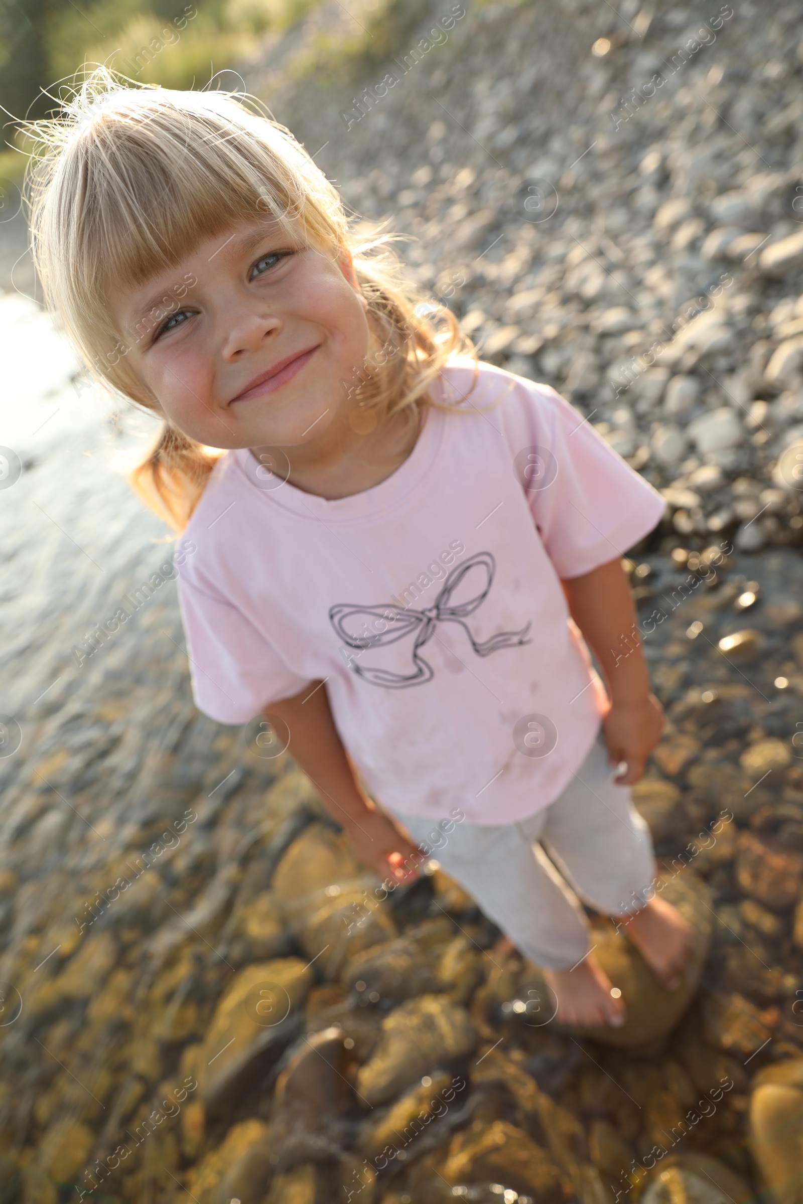 Photo of Cute little girl standing in water, above view. Child enjoying beautiful nature