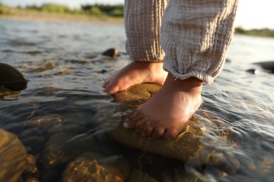 Cute little girl standing in water outdoors, closeup. Child enjoying beautiful nature