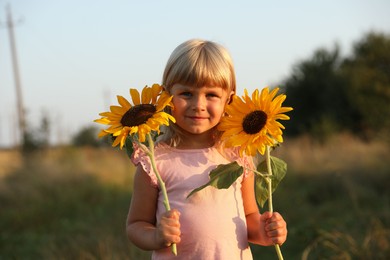 Photo of Little girl with sunflowers at meadow. Child enjoying beautiful nature