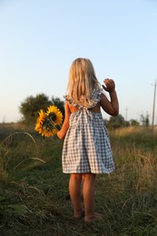 Little girl with sunflowers at meadow, back view. Child enjoying beautiful nature