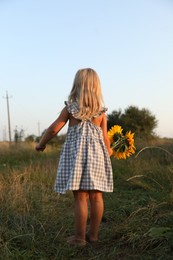 Little girl with sunflowers at meadow, back view. Child enjoying beautiful nature