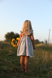 Photo of Little girl with sunflowers at meadow, back view. Child enjoying beautiful nature