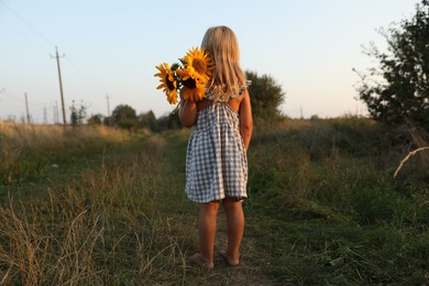 Photo of Little girl with sunflowers at meadow, back view. Child enjoying beautiful nature