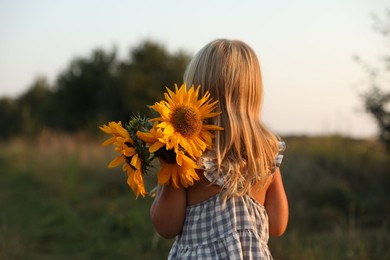 Little girl with sunflowers at meadow, back view. Child enjoying beautiful nature