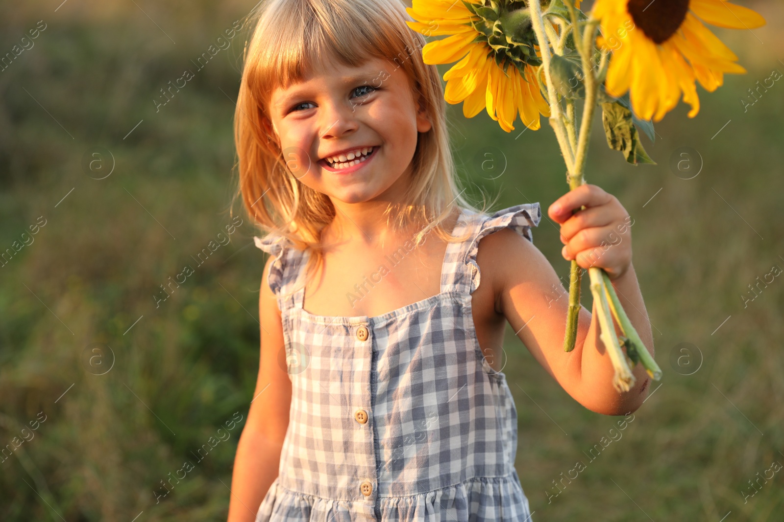 Photo of Little girl with sunflowers at meadow. Child enjoying beautiful nature