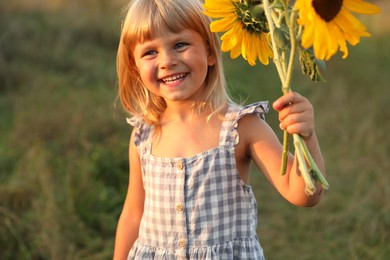 Little girl with sunflowers at meadow. Child enjoying beautiful nature