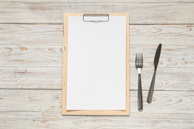 Photo of Clipboard with empty paper for menu design and cutlery on wooden table, flat lay