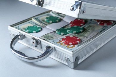 Photo of Metal case full of dollar banknotes and casino chips on light background, closeup