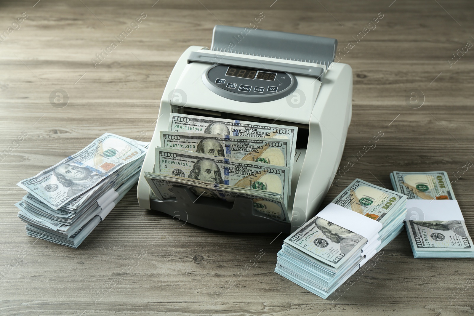 Photo of Money counter machine with dollar banknotes on wooden table